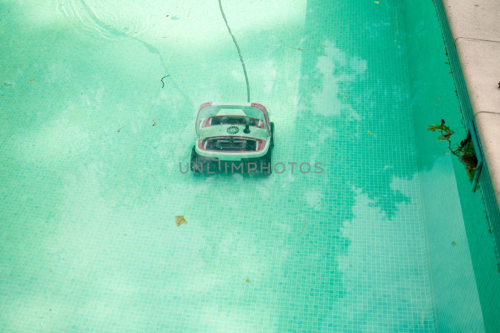 Water robot vacuum cleaner cleans, removes debris on the bottom, walls of the pool, top view through translucent water. Pool cleaning process. Preparing for the summer season. Smart home technologies