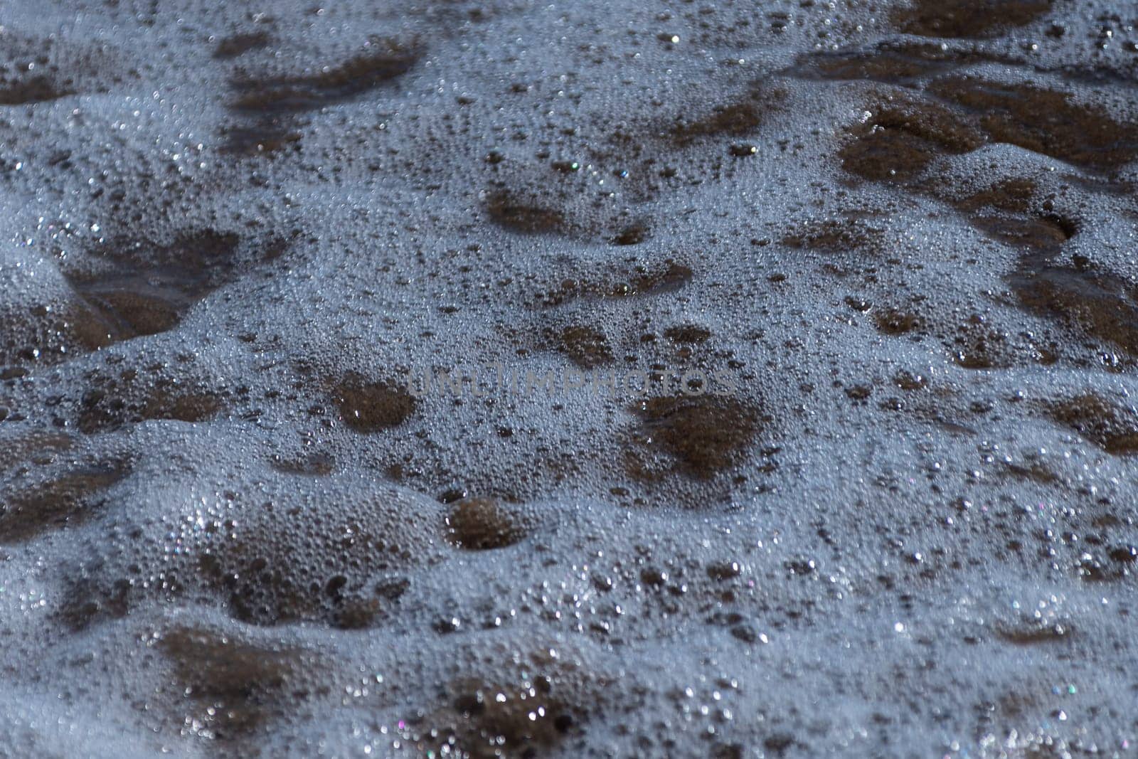 Detailed shot capturing foam from a breaking wave on sandy shore