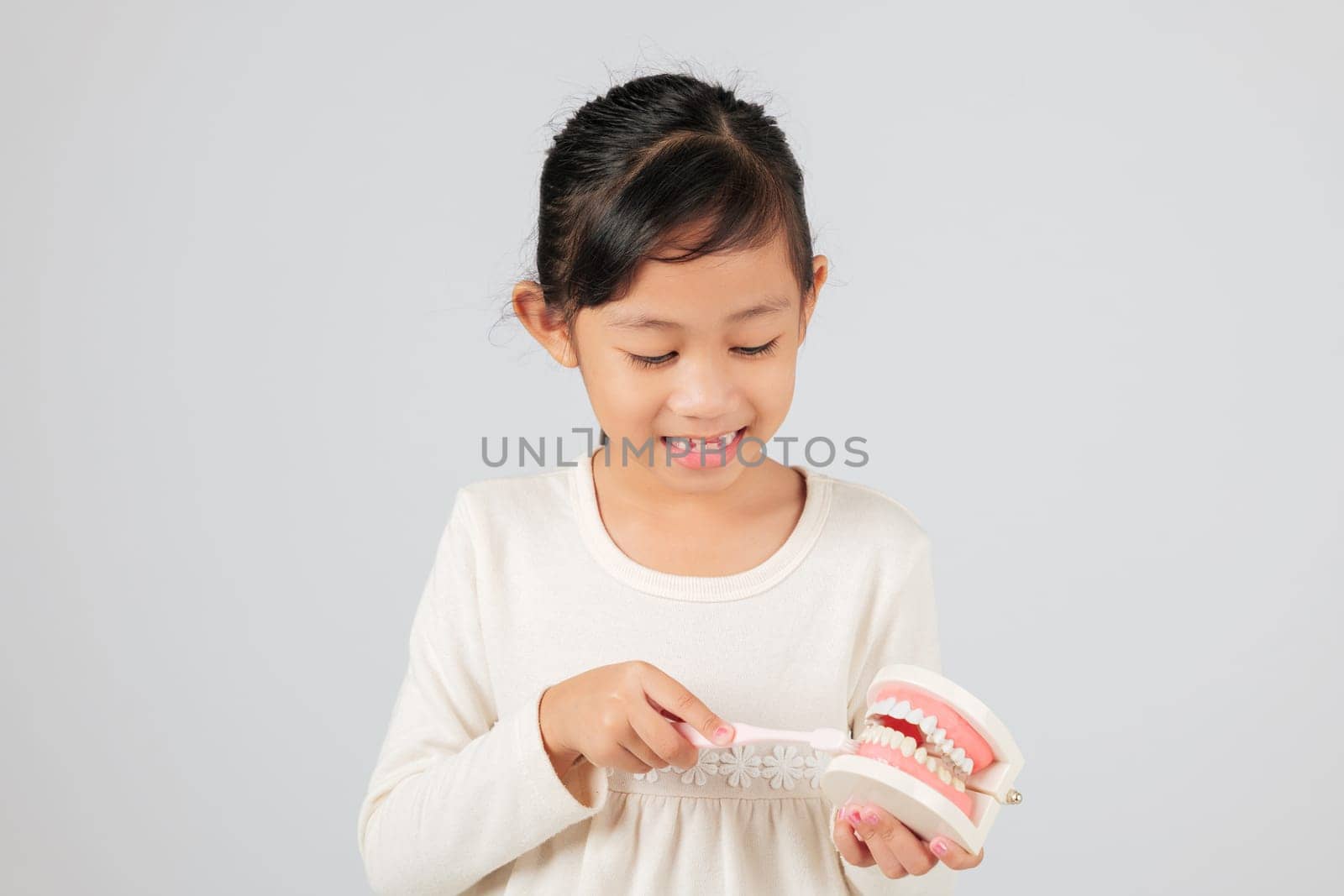 Dentist explains tooth loss to smiling girl holding toothbrush and teeth model. Asian kid with gap learns about milk teeth, dental care, and good hygiene. isolated white background