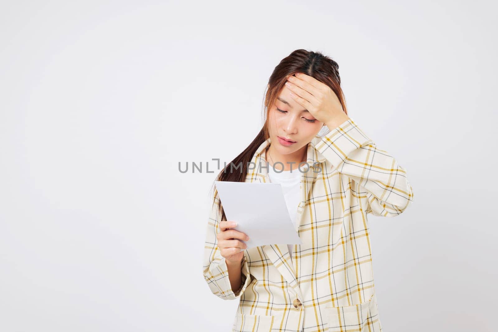 Financial stress overwhelms the Asian woman as she holds a bill in each hand, reviewing her financial troubles and unpaid bill stack with a worried face. isolated studio white background