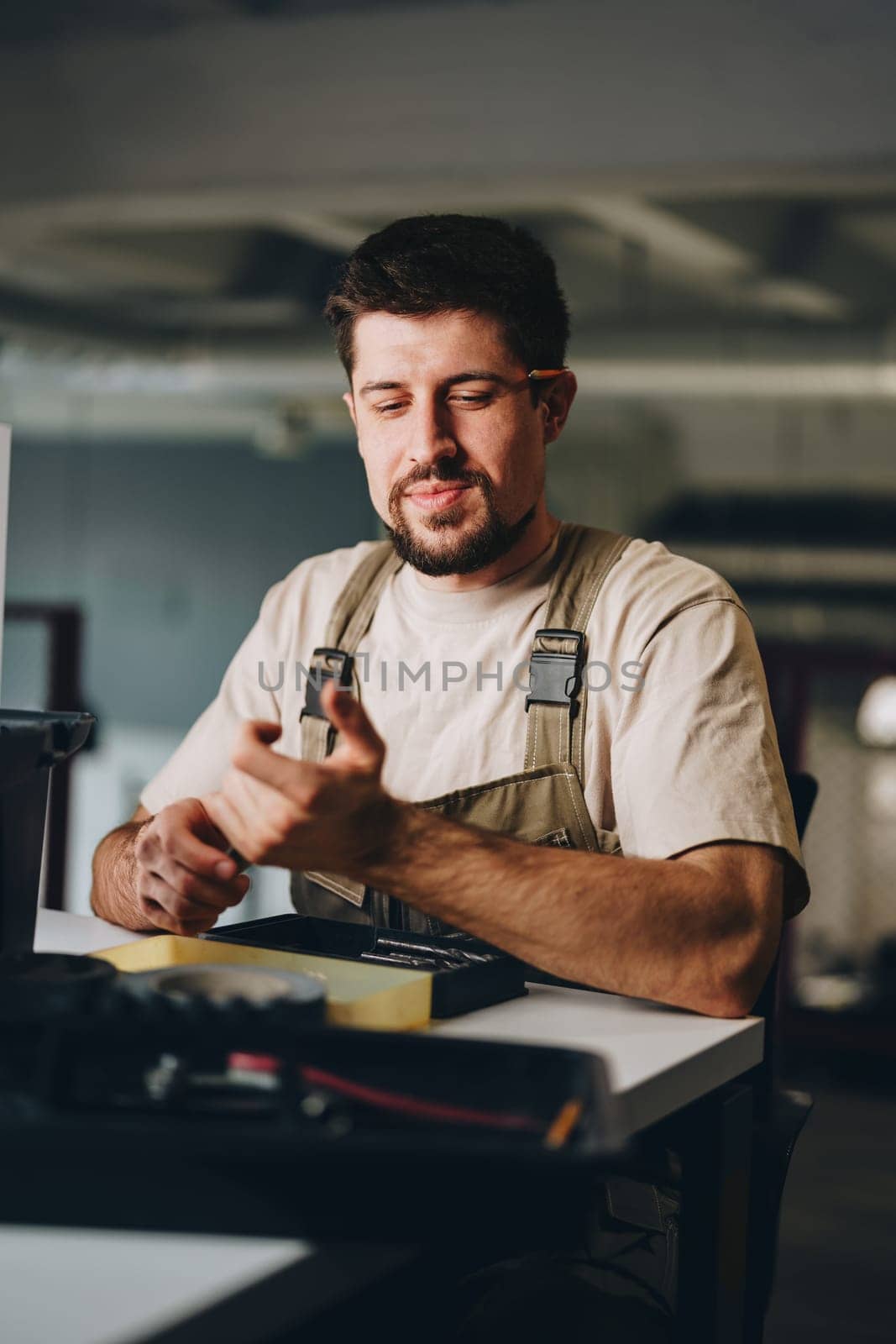 A focused craftsman checks his tools in a well-lit workspace. He holds a drill while surrounded by various equipment and materials, showing dedication to his craft.