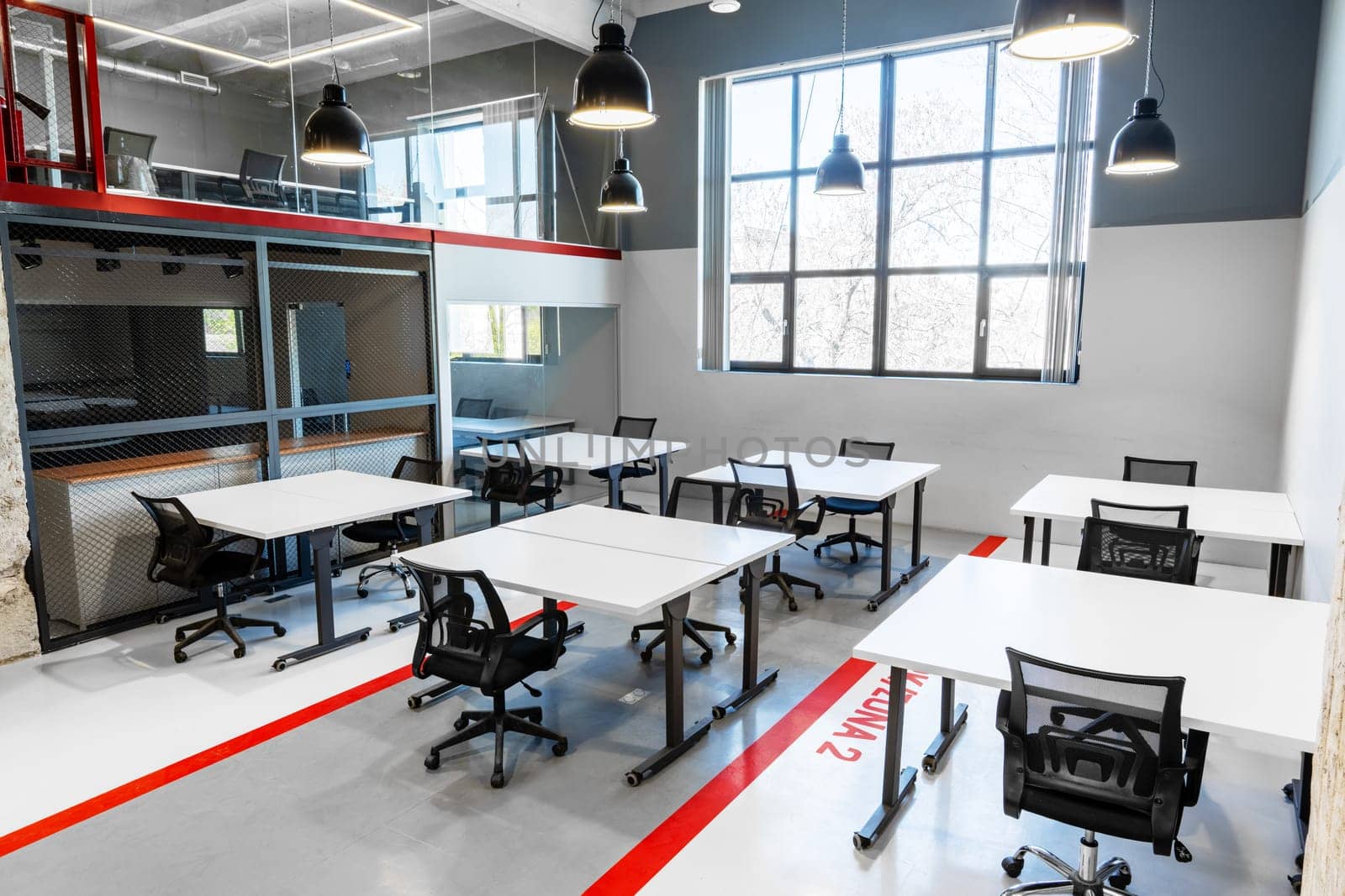 Bright and airy workspace featuring several desks and chairs arranged for collaborative work. Large windows let in natural light, enhancing the modern design and feel.