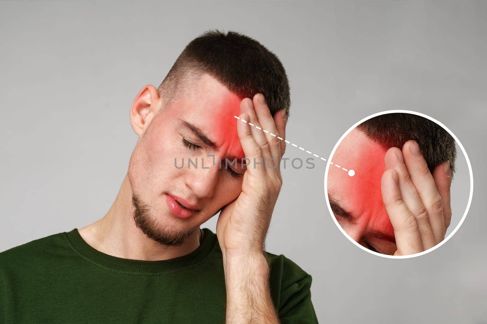 A young man holds his forehead in pain, indicating a headache. His expression shows visible discomfort while he stands in a brightly lit indoor environment.
