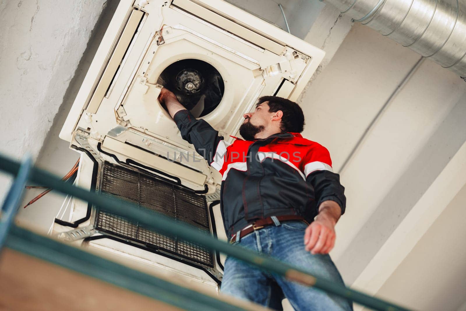 A technician is working on an air conditioning unit mounted on the ceiling of a commercial space. The professional is adjusting components, ensuring optimal functionality.
