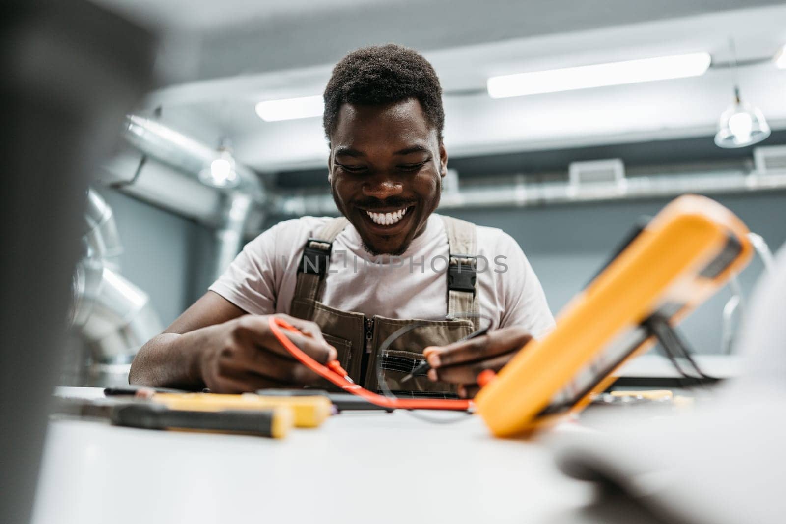 A cheerful technician engages in electrical work in a modern workshop. Equipped with various tools, he meticulously tests and adjusts components, showcasing his expertise and dedication.