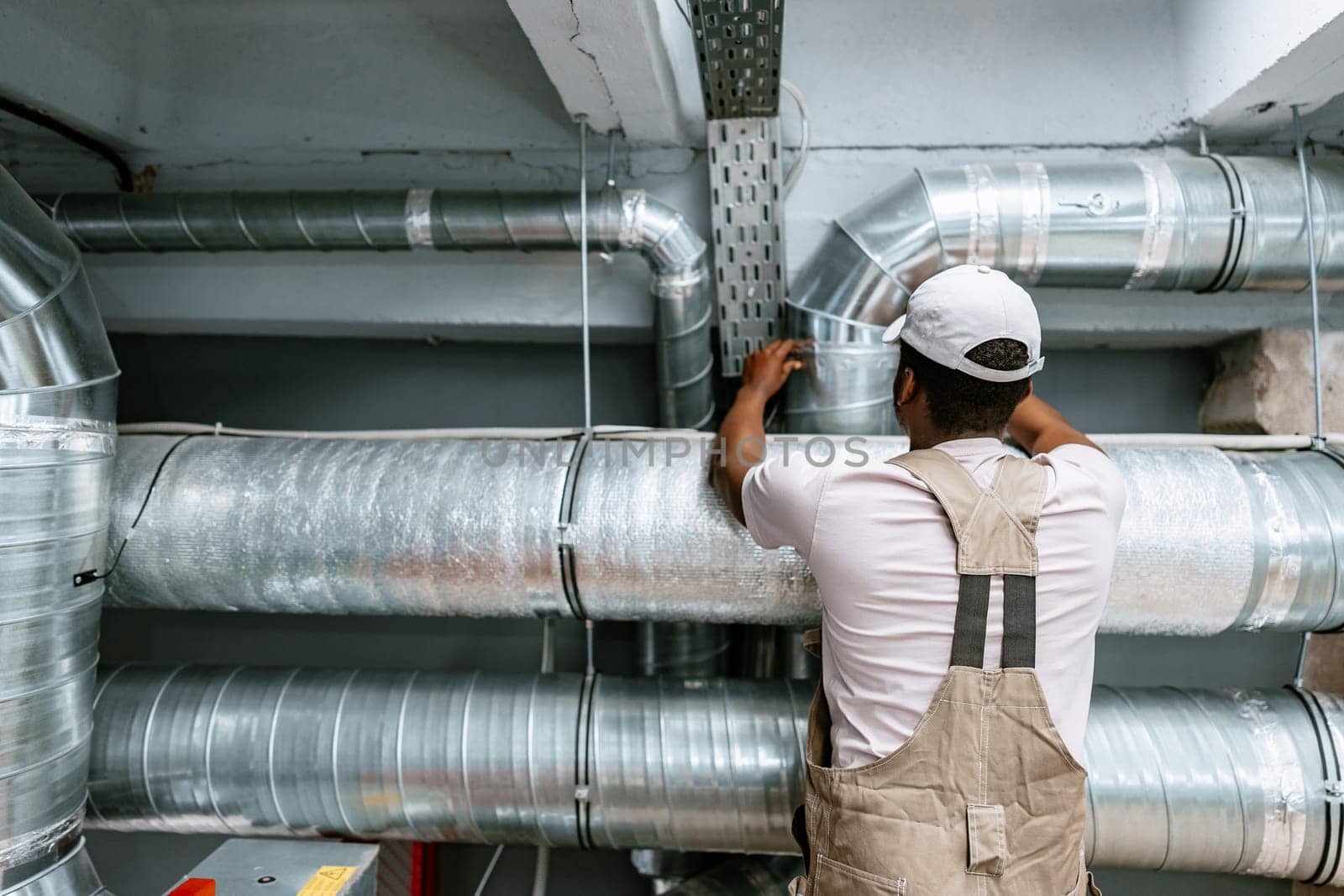 A technician is working diligently to install metal ducting in a commercial building, ensuring proper air circulation and system efficiency. This project takes place indoors.