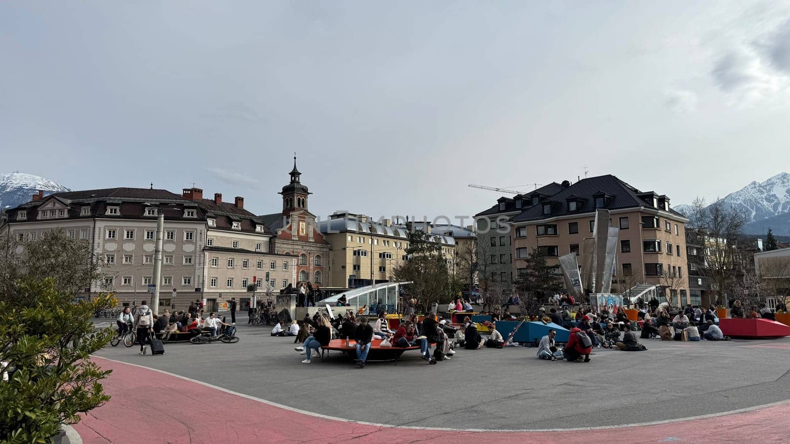 Innsbruck, Austria - March 28, 2025: Public square in Innsbruck, Austria bustling with people enjoying leisure activities, surrounded by historic buildings and mountains