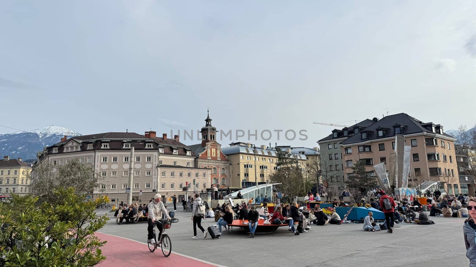 Innsbruck, Austria - March 28, 2025: City square in Innsbruck bustling with people, historic architecture, and stunning mountain views, showcasing urban life