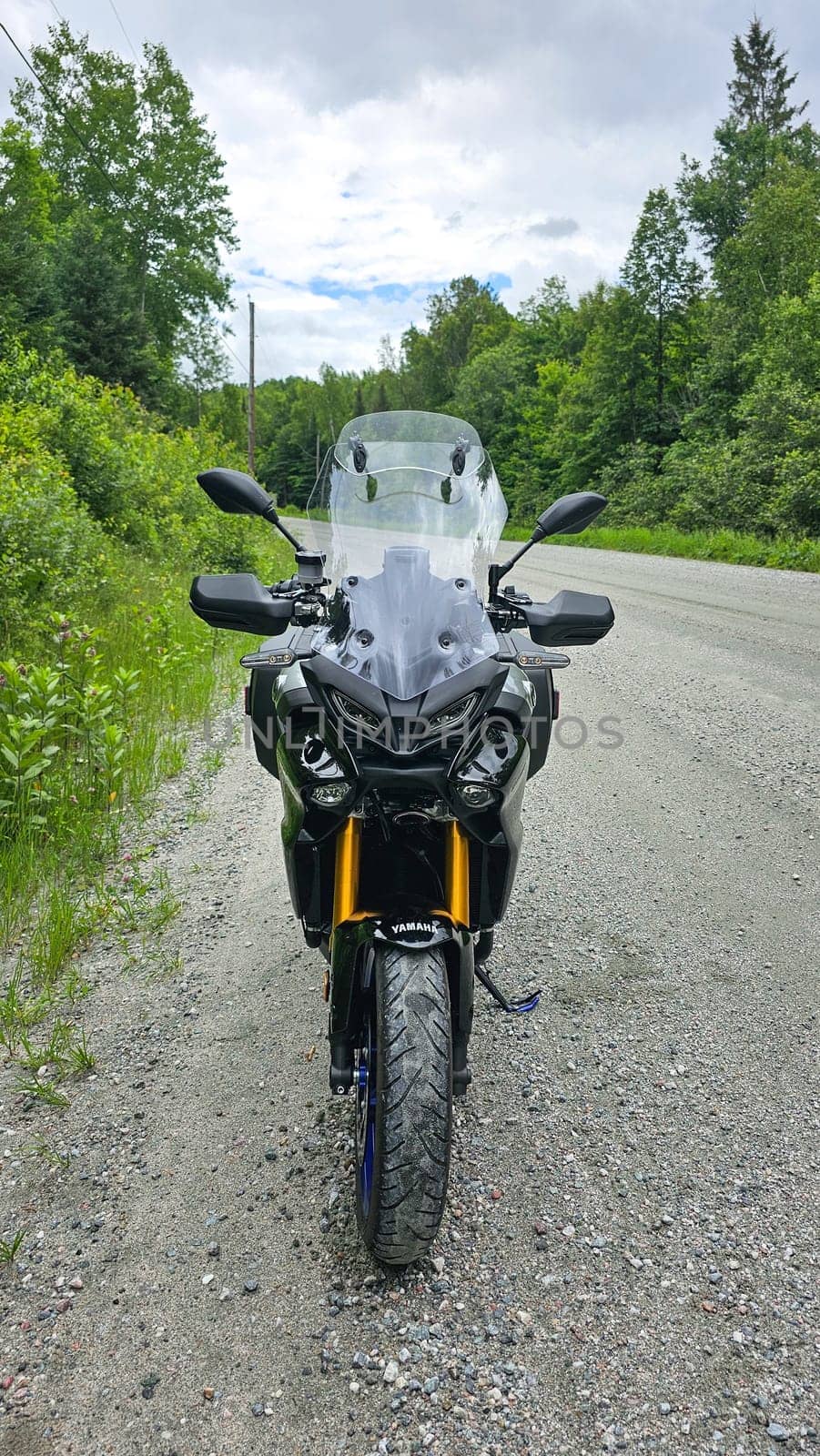 Sargent s Purchase, NH USA - 08.22.2024: Adventure Motorcycle Yamaha Tracer 9 GT on a Gravel Road Surrounded by Lush Greenery, Cloudy Sky Above.