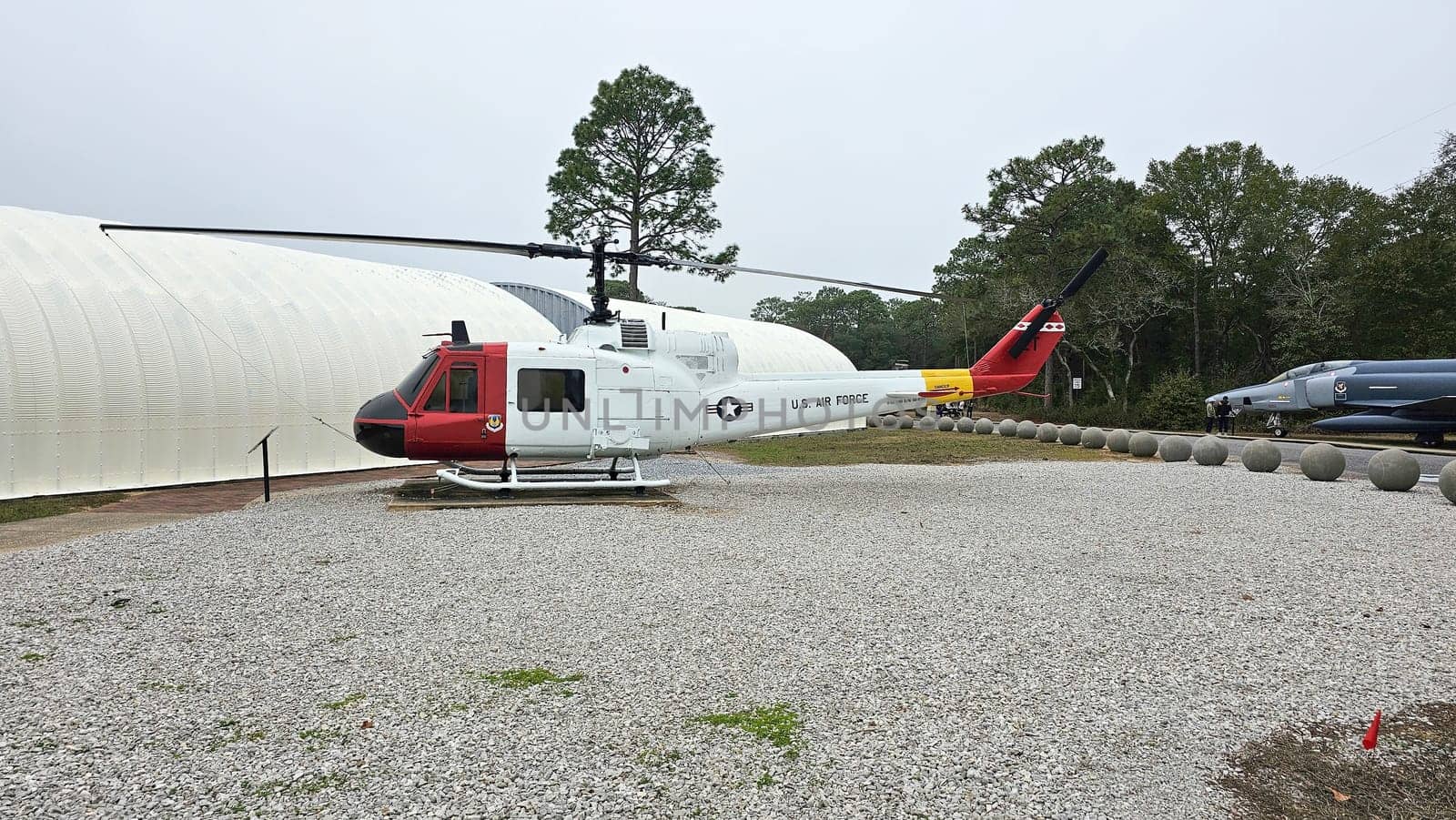 Eglin AFB, FL USA - 12.27.2024: Vintage Helicopter Displayed Outdoors with Unique Red and Yellow Tail Design, and Gray Gravel.