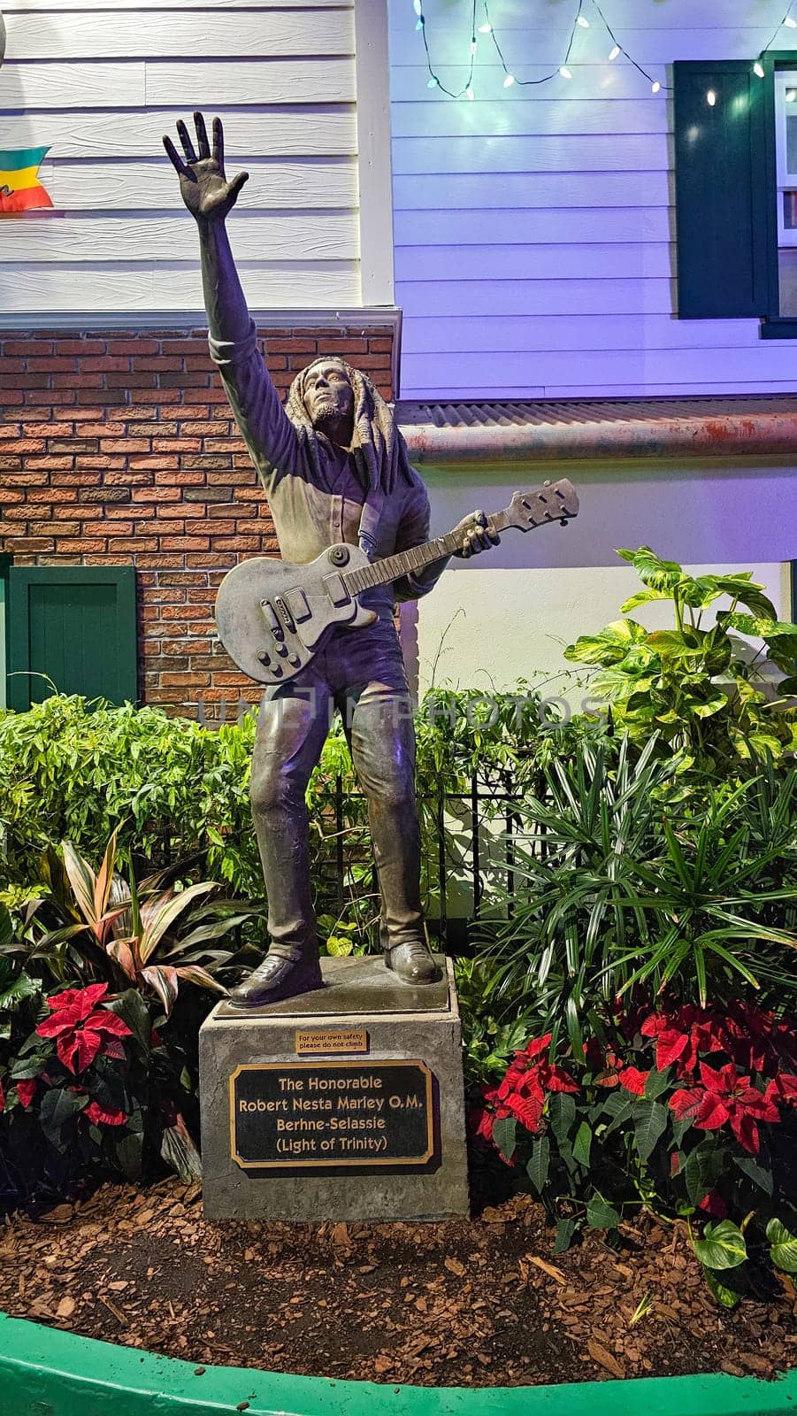 Orlando, FL USA - 12.31.2024: Bronze Statue of a Musician with Guitar and Raised Hand in a Garden Setting, Island.