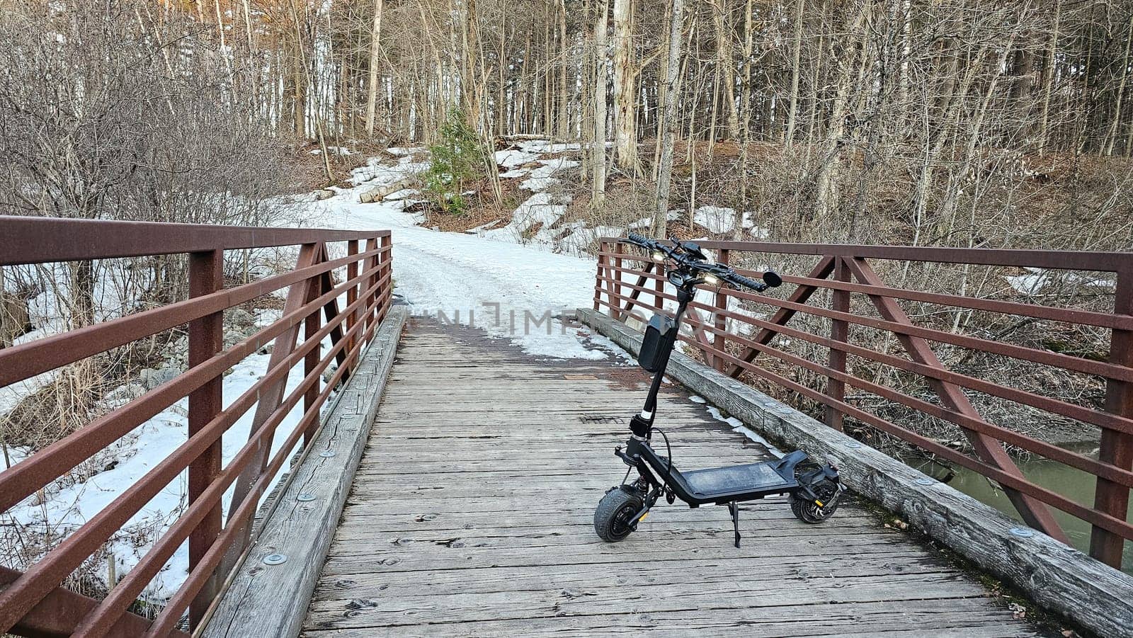 An electric scooter is parked on a wooden bridge amidst a wintry landscape, symbolizing eco-friendly travel and adventure in nature. Perfect for promoting sustainable tourism.