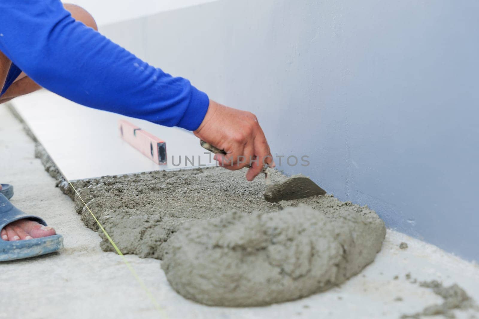 A worker hand uses a trowel to smooth gray mortar, preparing a level surface for floor tiles. Precision and craftsmanship in tiling work are on display.
