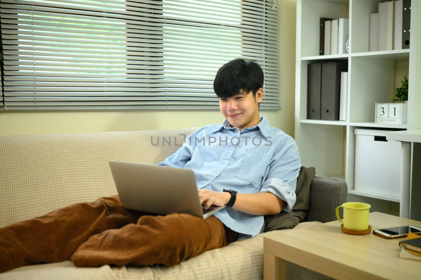 Young man relaxing on sofa using laptop at home remote work or online entertainment.