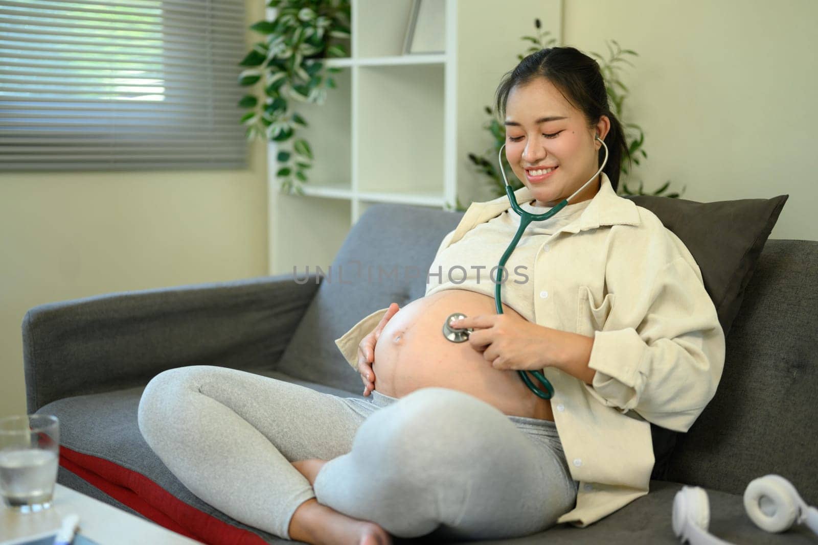 Pregnant woman using a stethoscope to listen to her baby heartbeat at home.