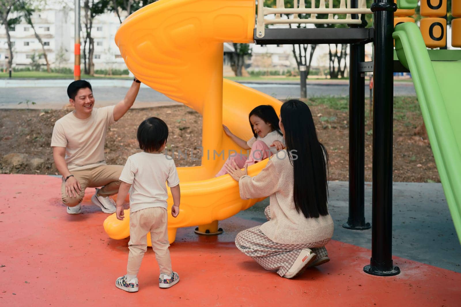 Smiling parents and two young children enjoy playtime at a colorful playground.
