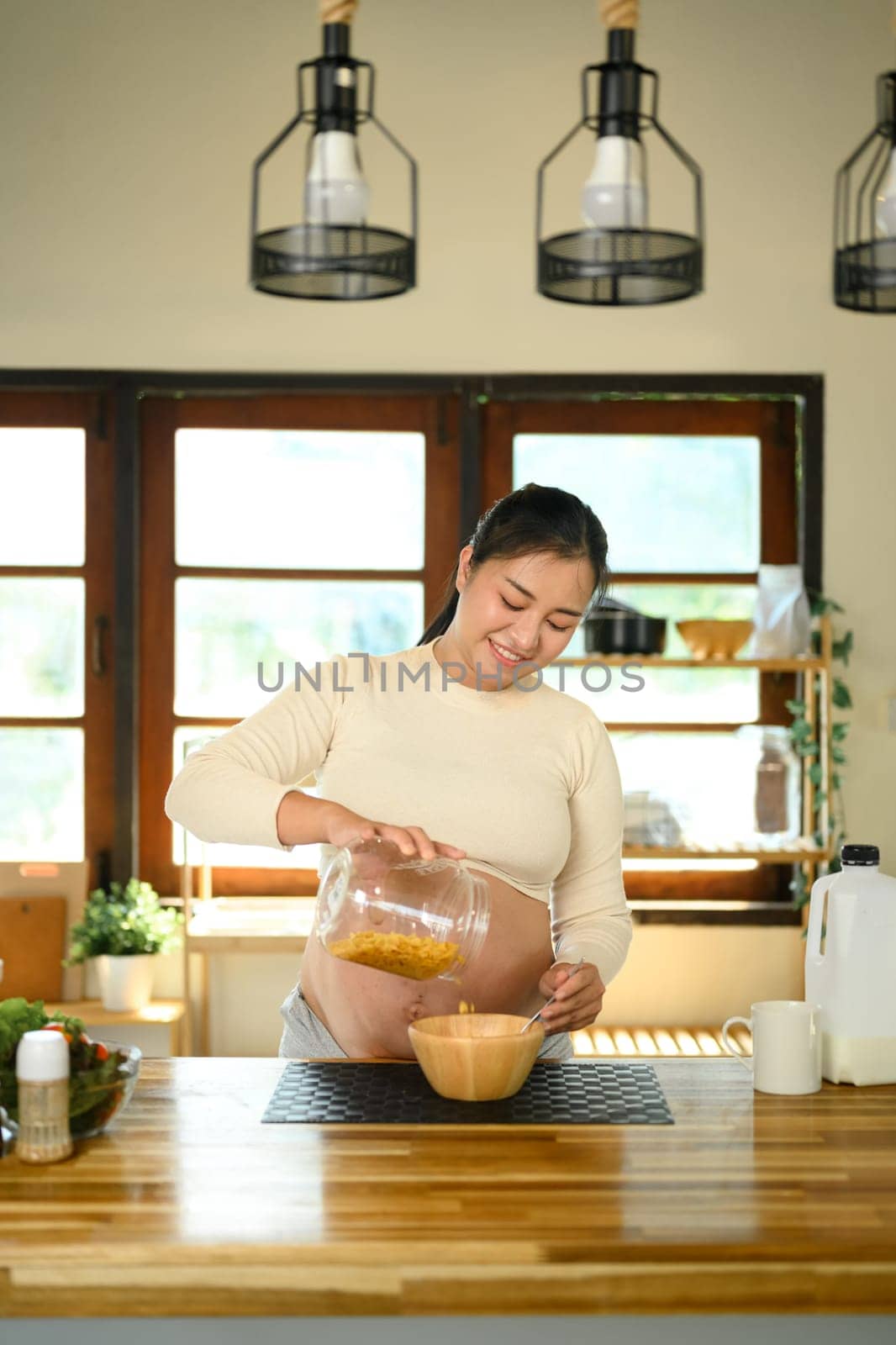 Asian pregnant woman preparing a light meal in a bright kitchen.