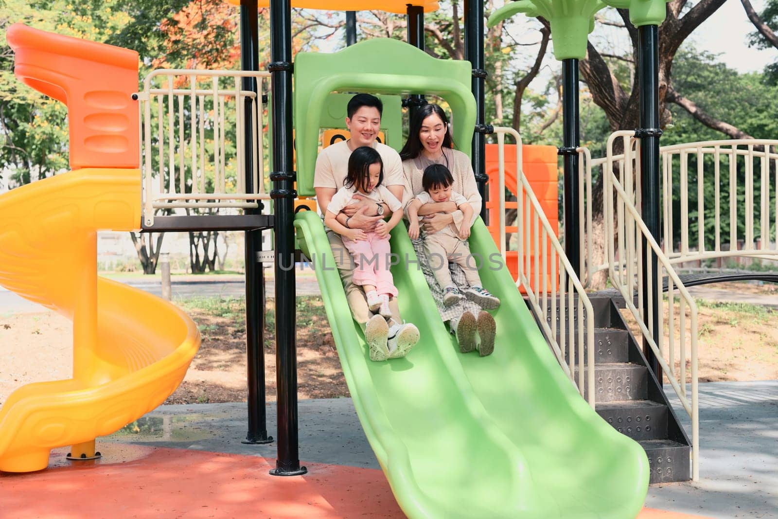 Happy family sliding down together at a colorful playground.