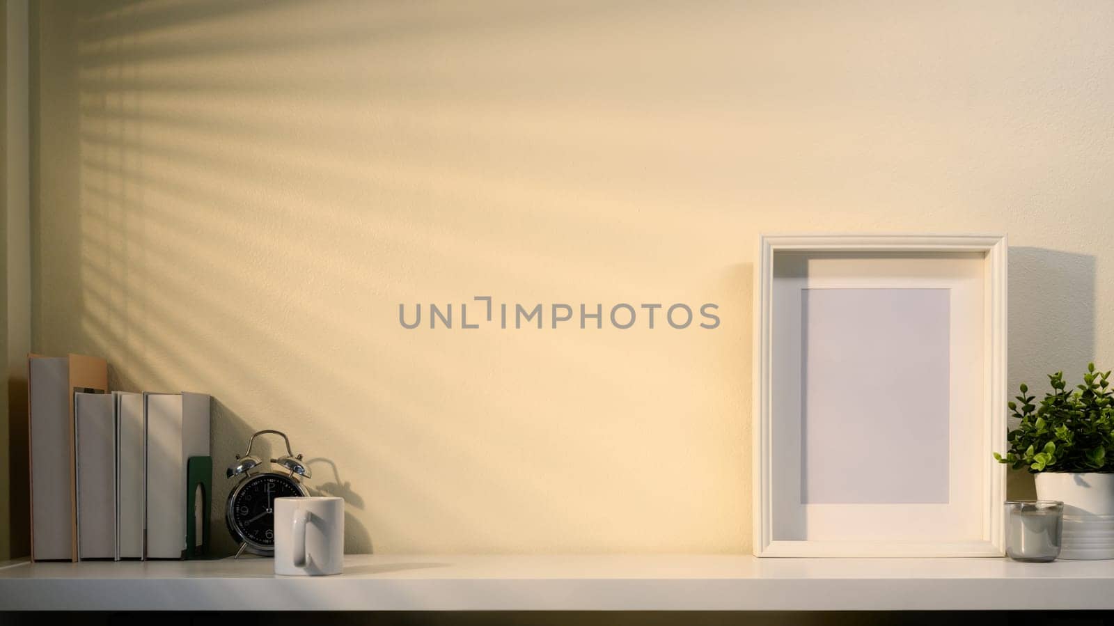 Minimalist workspace with empty frame, plants, books, and accessories in soft morning light.