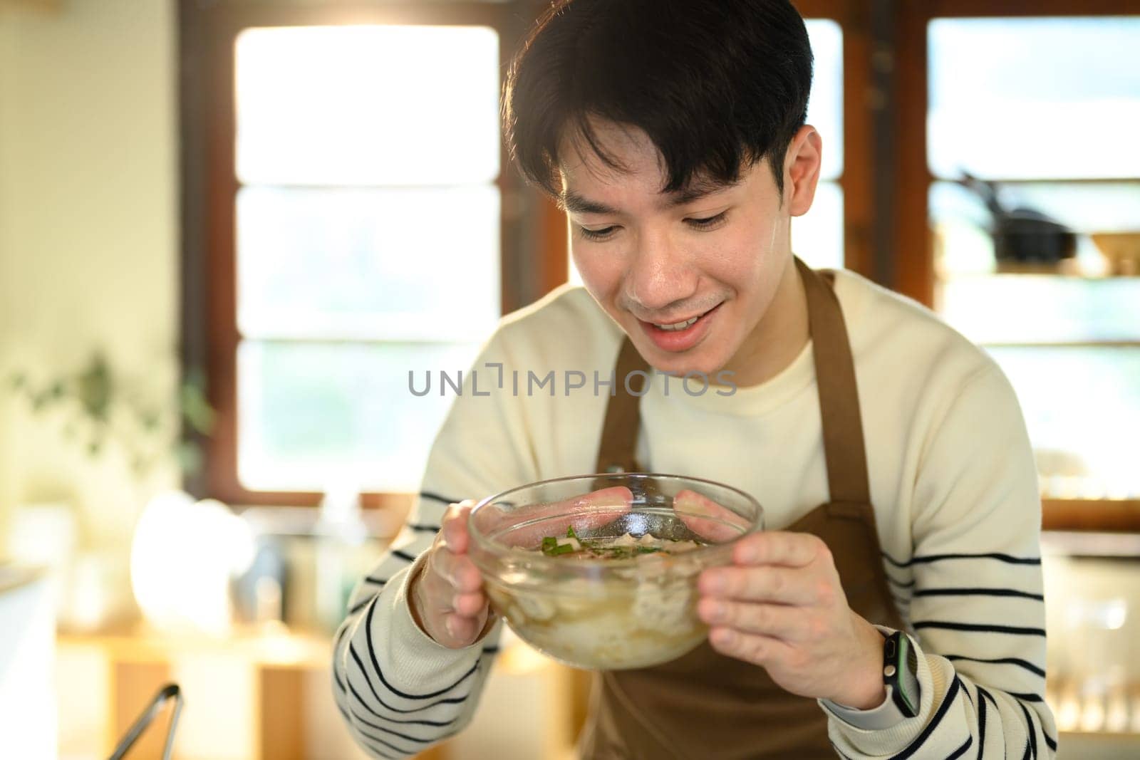 Happy asian man presenting a freshly prepared bowl of noodle soup.