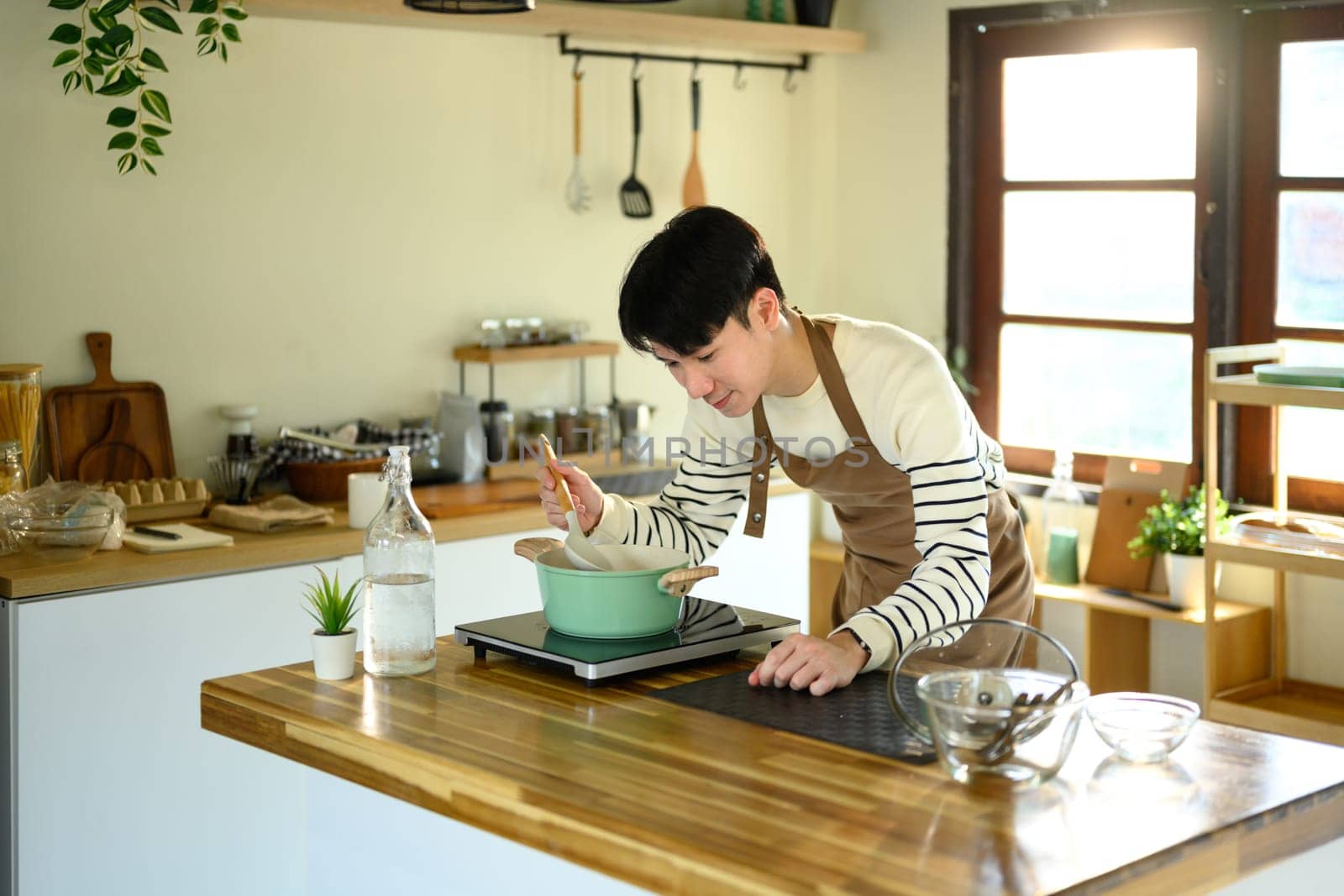 Happy Asian man preparing a meal on a modern stovetop.