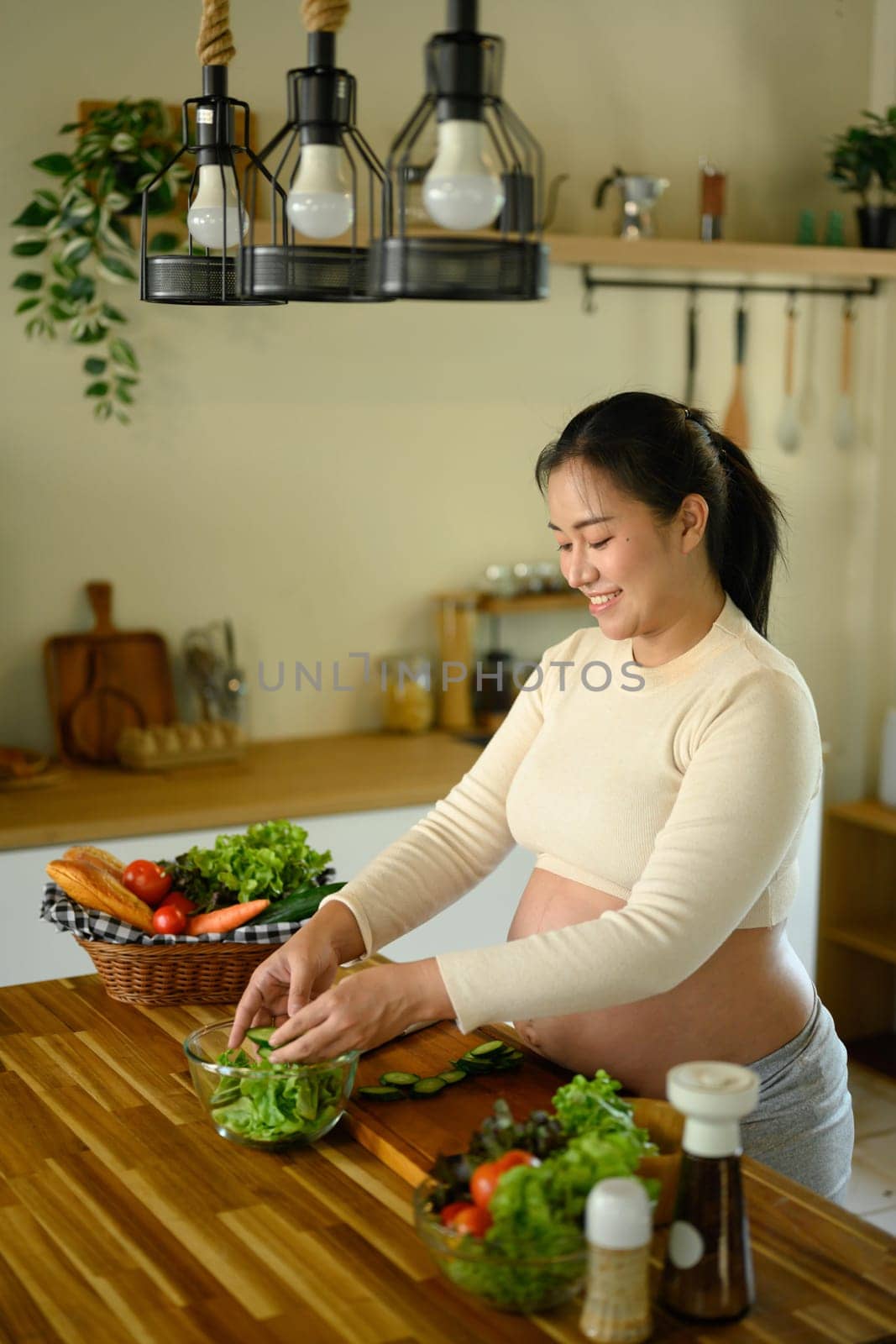Expecting mother preparing a salad with fresh vegetables in home kitchen.