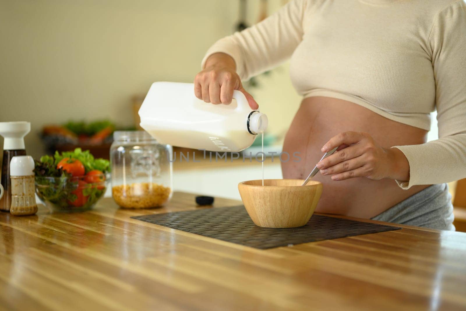 Hands of a pregnant woman making a morning meal in a bright kitchen.