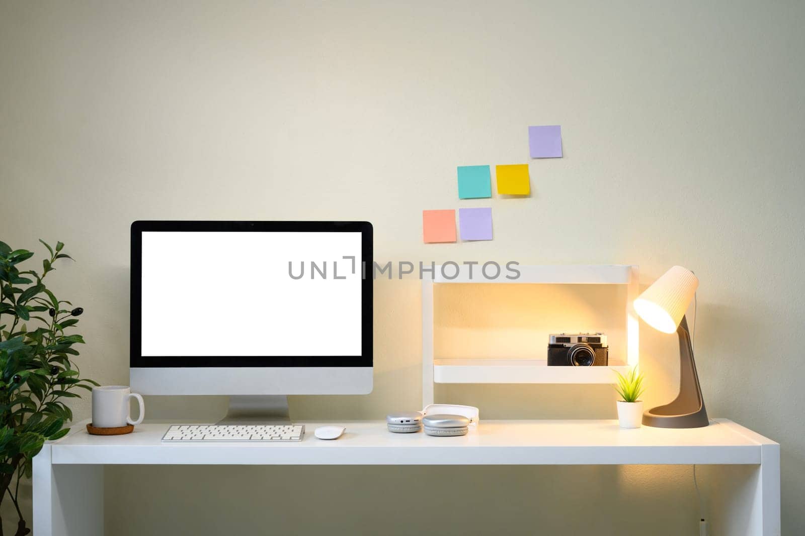 Modern workspace with desktop monitor, sticky notes on wall, desk lamp, and creative decor.