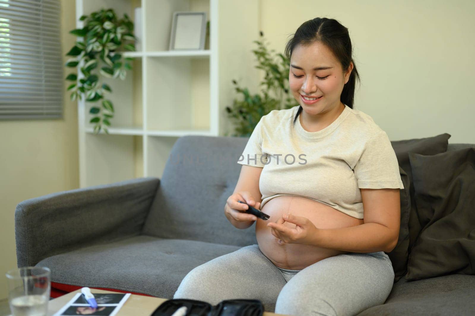 Pregnant woman taking a blood sugar test in a living room.