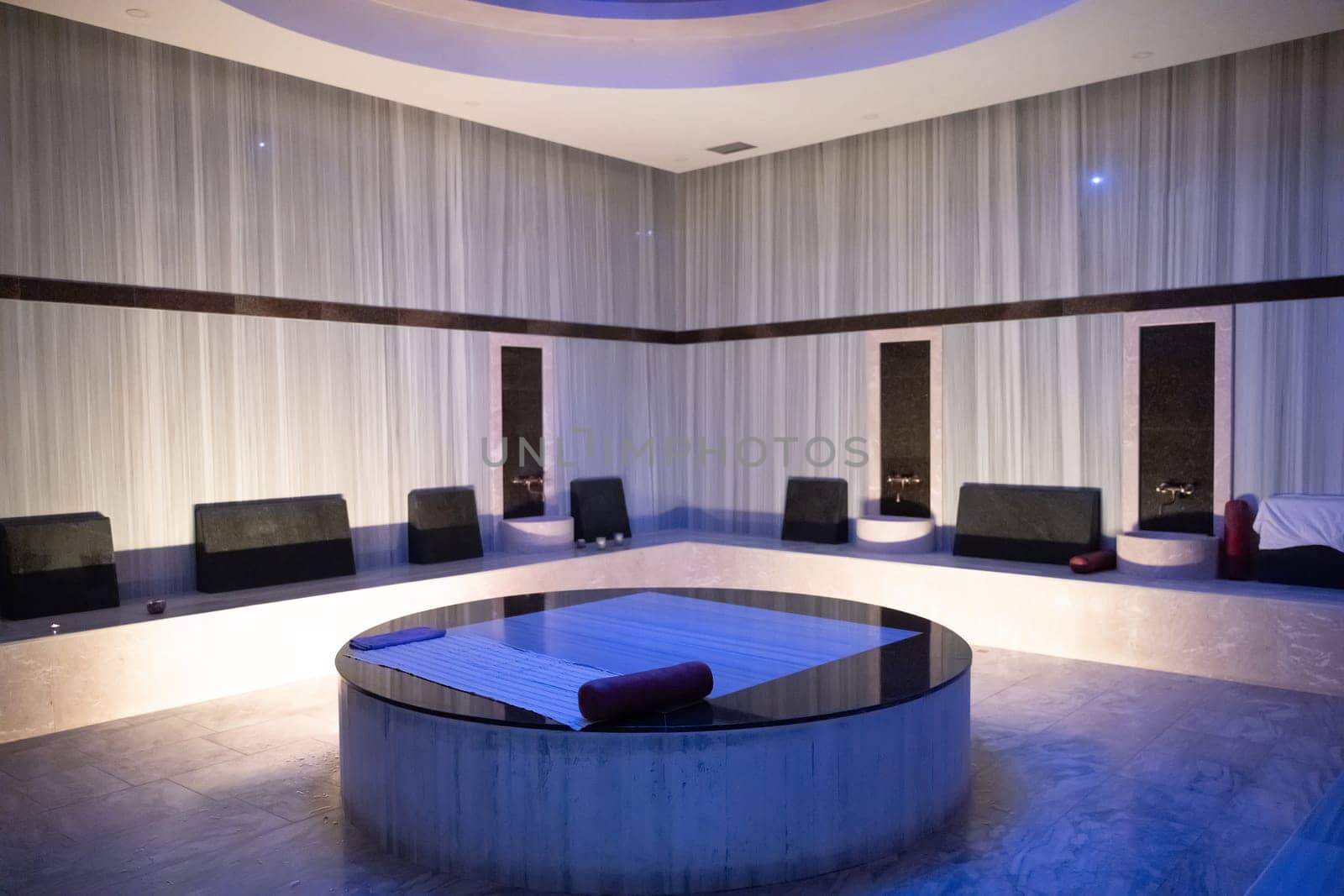 Modern Hammam Room with Stone Table. Modern hammam steam room with a central round stone massage table and stylish decor.