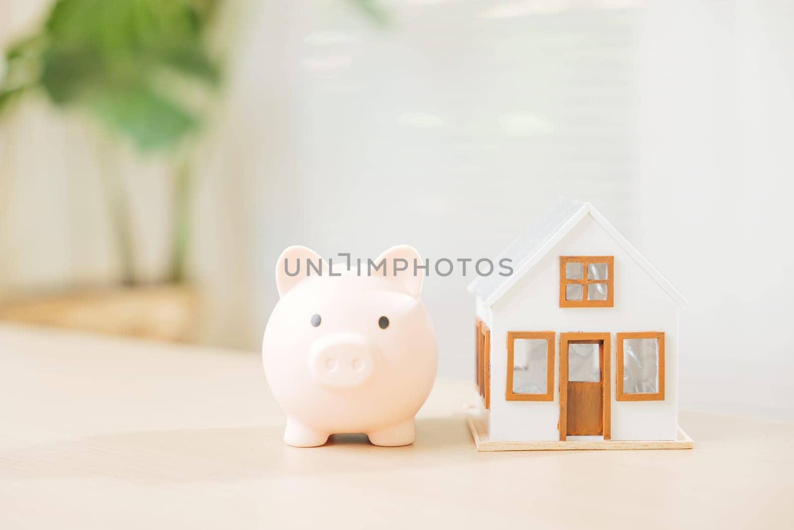 A piggy bank and white house model sit on a table, symbolizing saving money for property investment. Explore real estate opportunities, dream home buying, and smart mortgage planning.