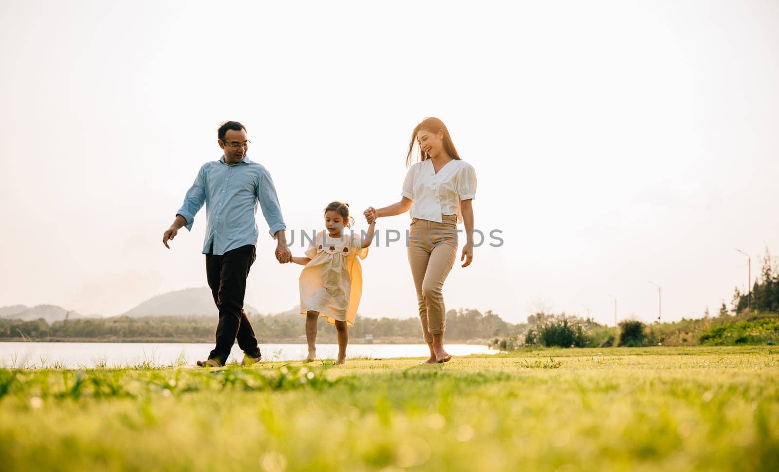 A cute Asian little girl with her mother and father walking and holding hands in a beautiful park, enjoying the nature and the season of spring, Happy family day