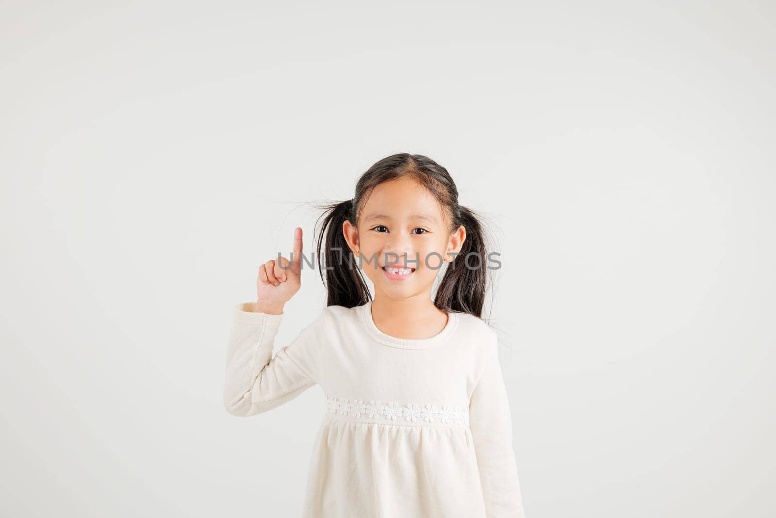 Asian happy portrait cute young kid girl makes gesture fingers point upwards above presenting product something, studio shot isolated on white background, kindergarten children woman smile