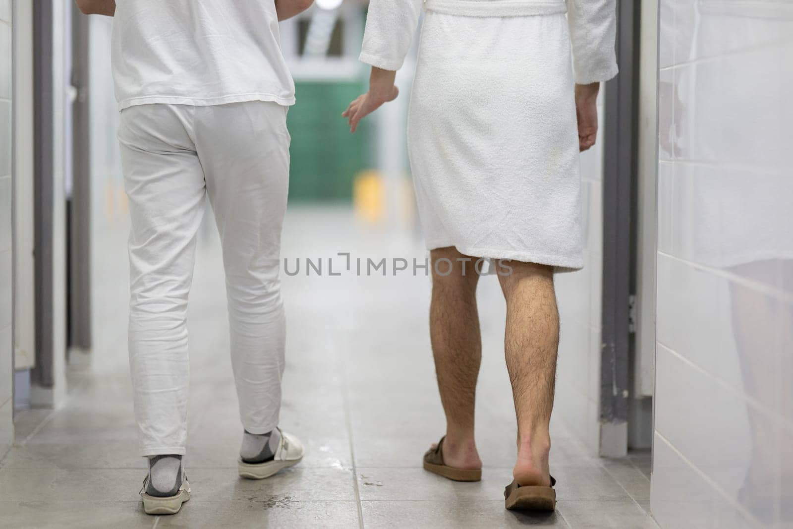 Medical Consultation in Spa Corridor.Two men discussing treatment options while walking through a clinical spa corridor, wearing white uniforms and bathrobe