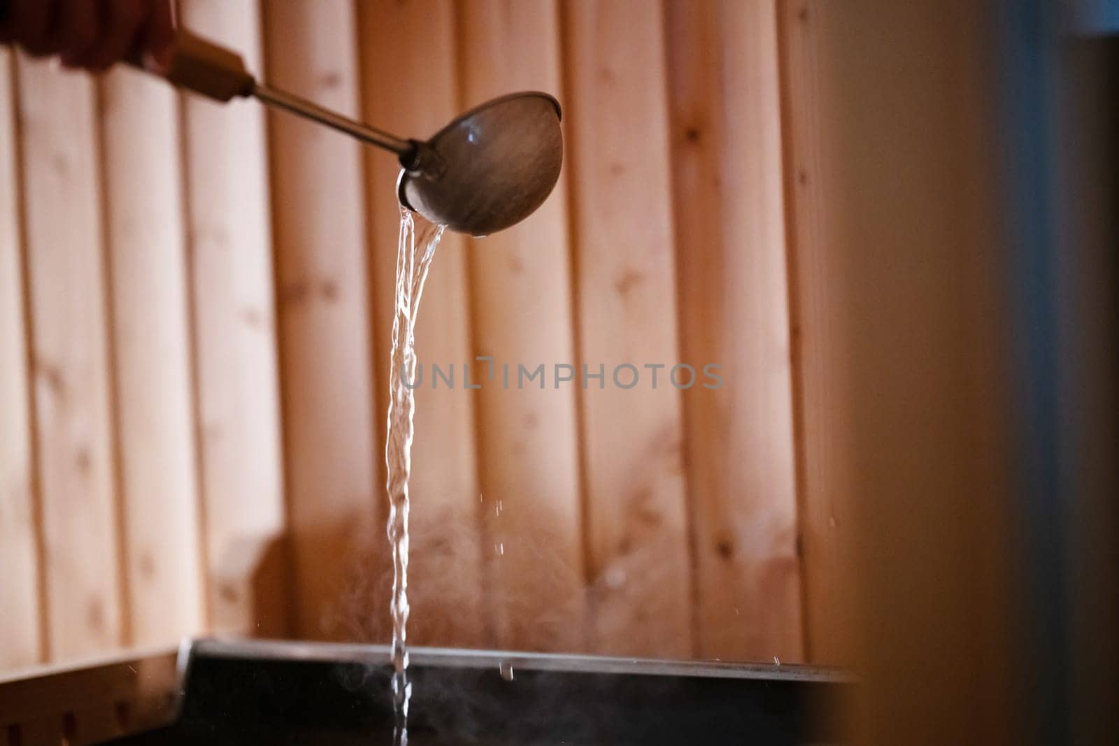 Detailed close up of sauna bucket with ladle and essential oils next to rolled towels on wooden bench inside sauna.