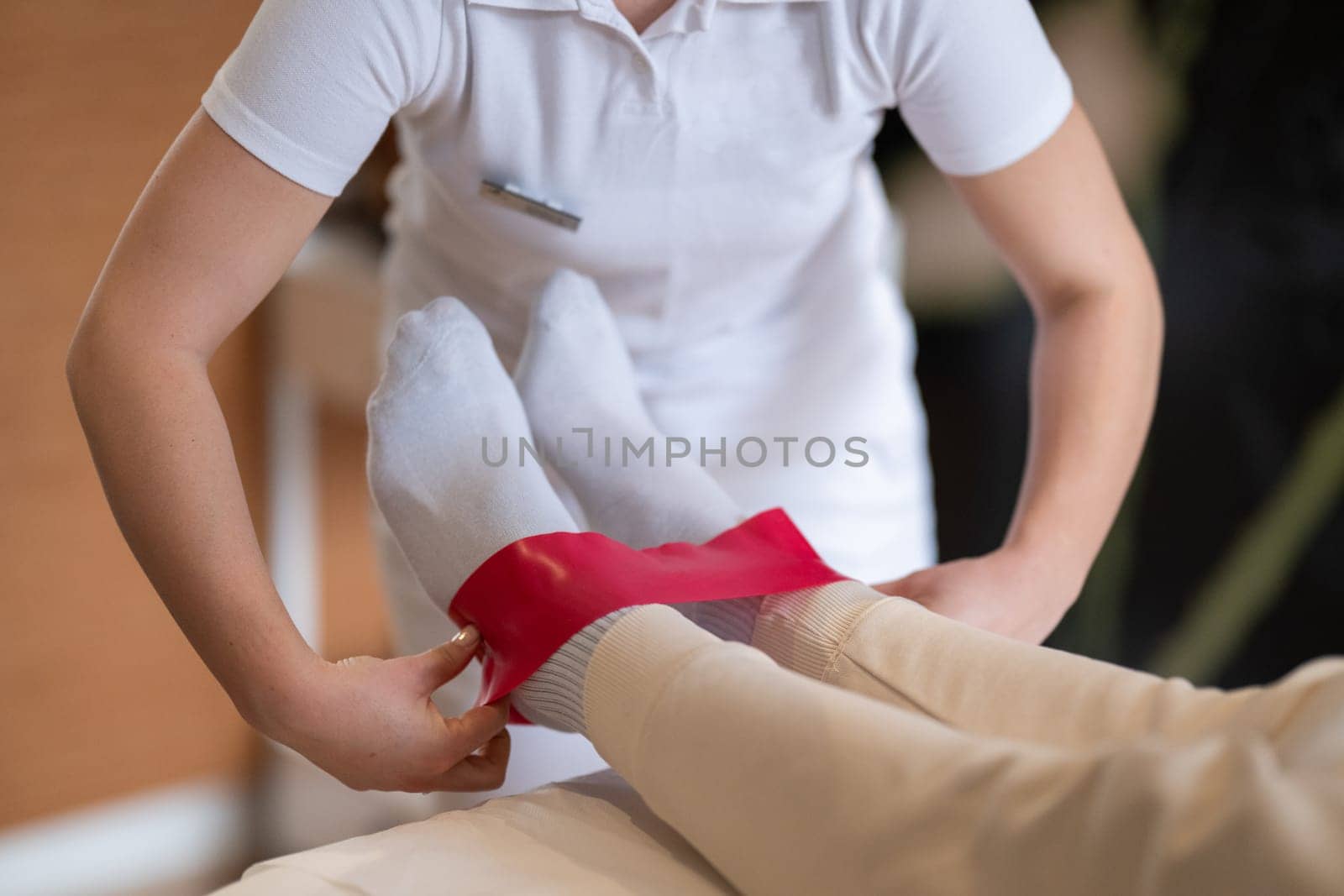 Close up view of a physiotherapist applying a red resistance band around a patient's ankles during a leg therapy session.