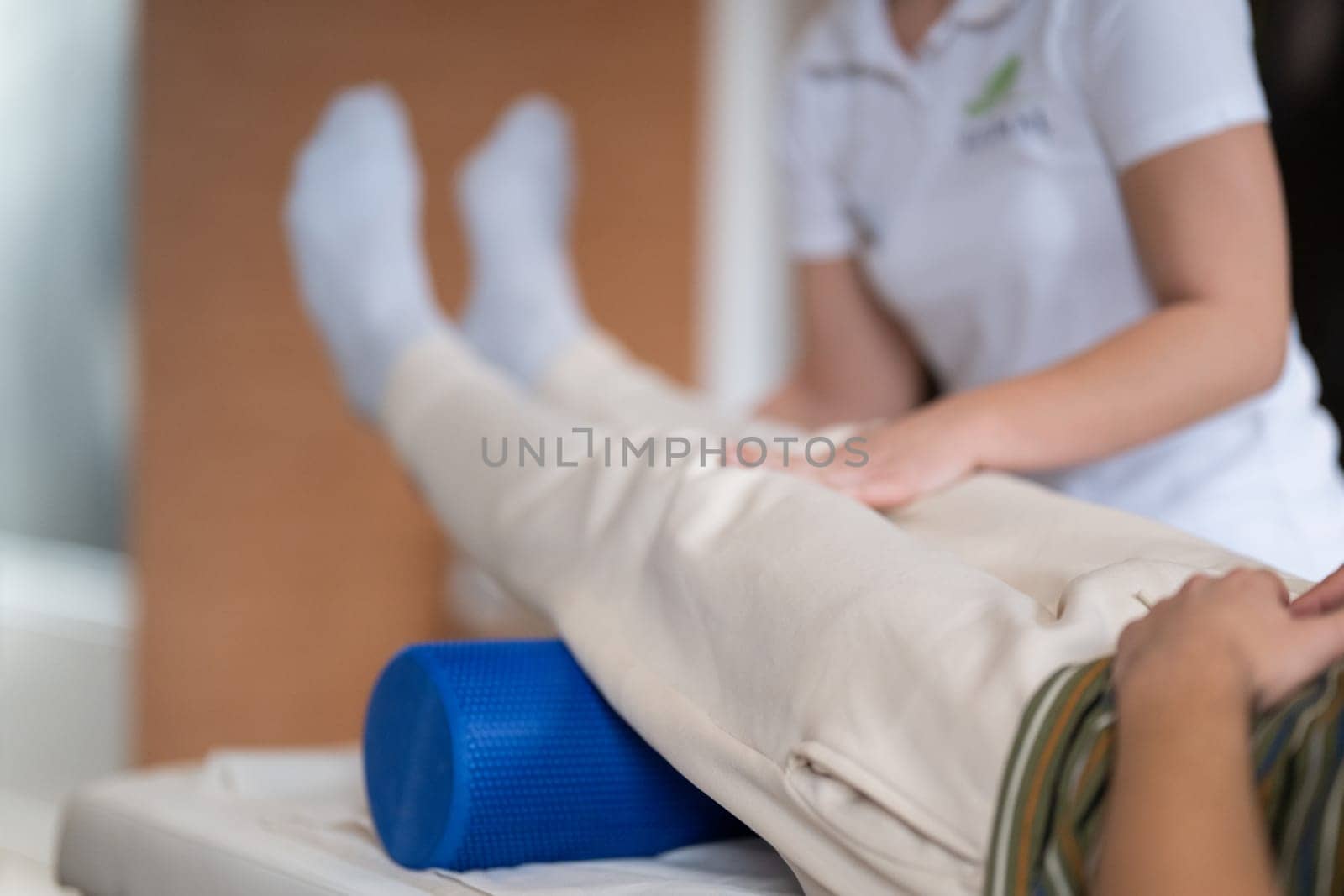 A therapist guiding a patient through leg exercises with the help of a blue foam roller in a therapy clinic.