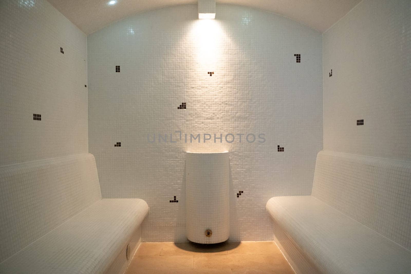 Clean and minimalistic steam room with tiled walls and benches, featuring soft lighting and a central water fixture.