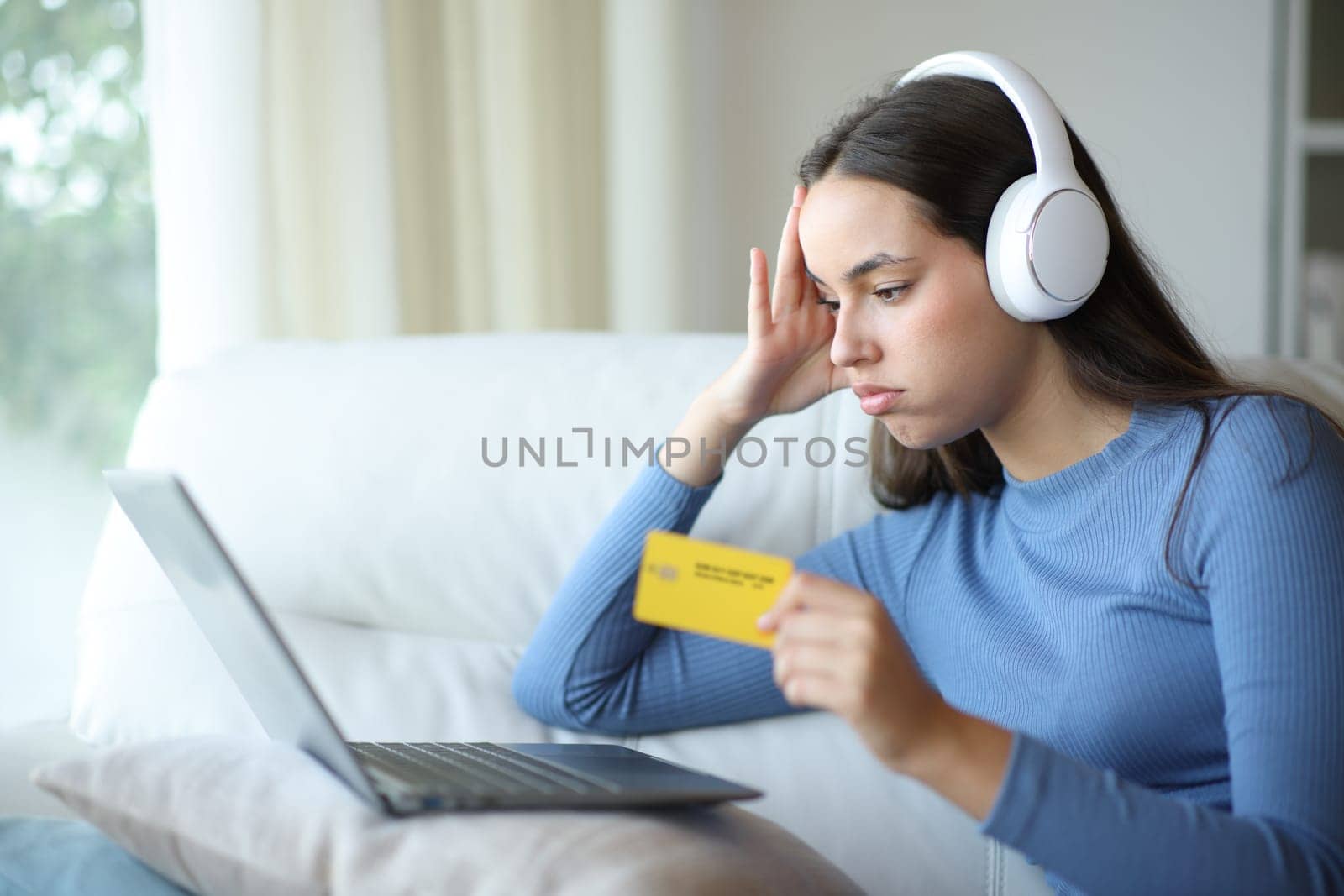 Frustrated woman wearing headphone buying entertainment content after mistake sitting on a couch at home