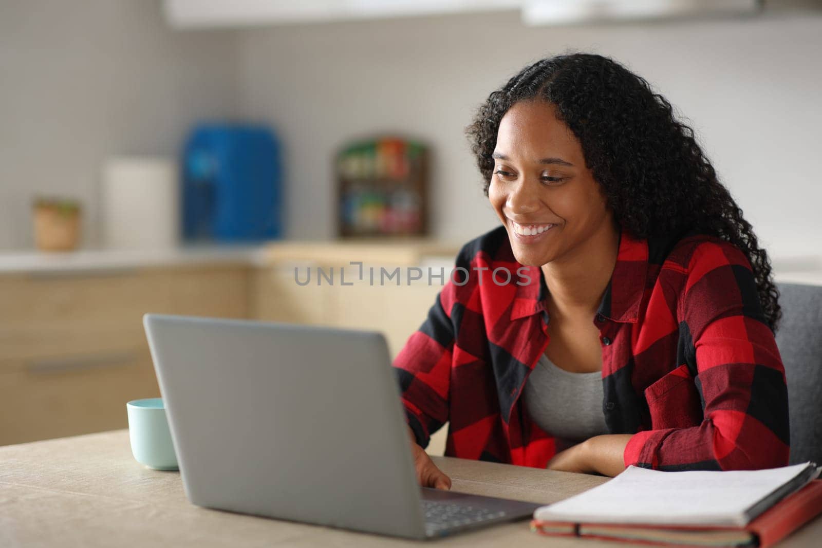 Happy black student e-learning using laptop in a kitchen at home