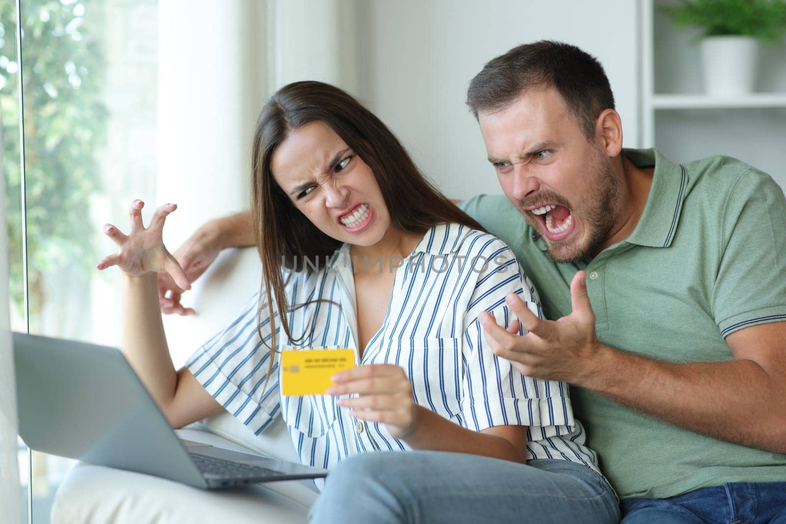Angry couple of consumers trying to buy online using credit card and laptop sitting on a couch at home