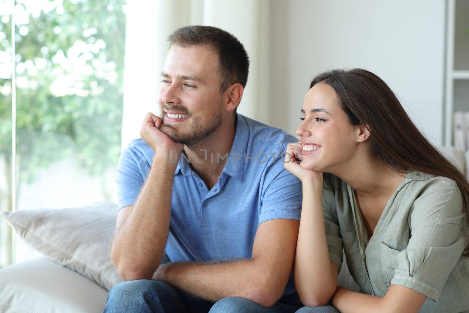 Happy relaxed couple looking through a window sitting on a couch at home