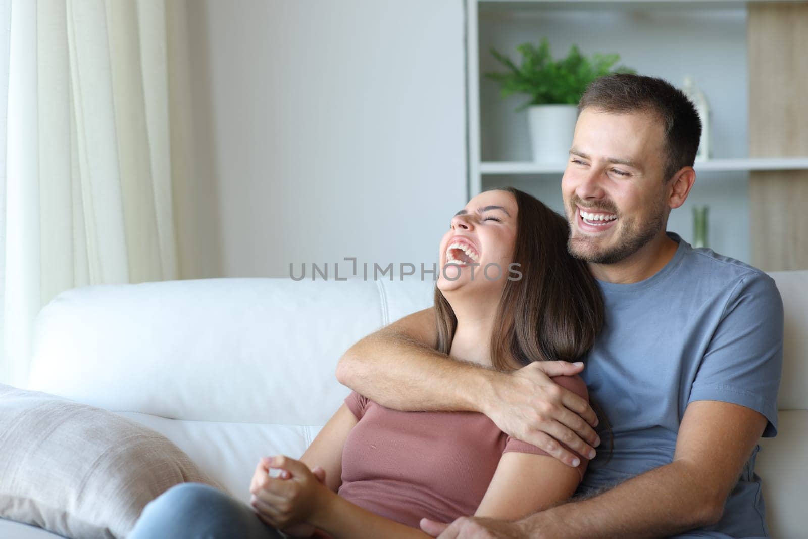 Couple laughing loud being happy sitting on a couch at home