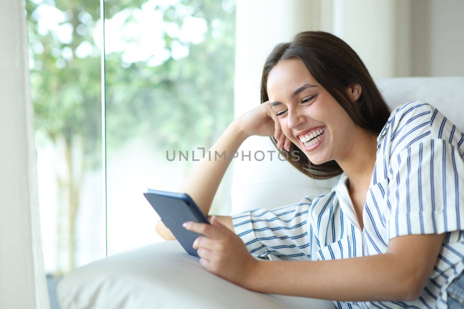 Happy woman reading ebook relaxing sitting on a couch at home