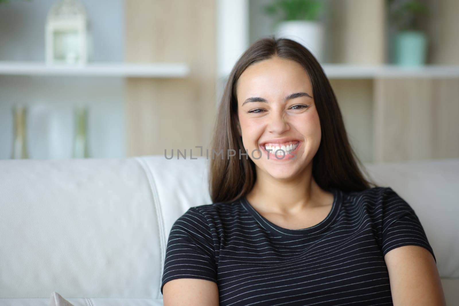 Happy woman with perfect smile looks at camera sitting on a couch in a house