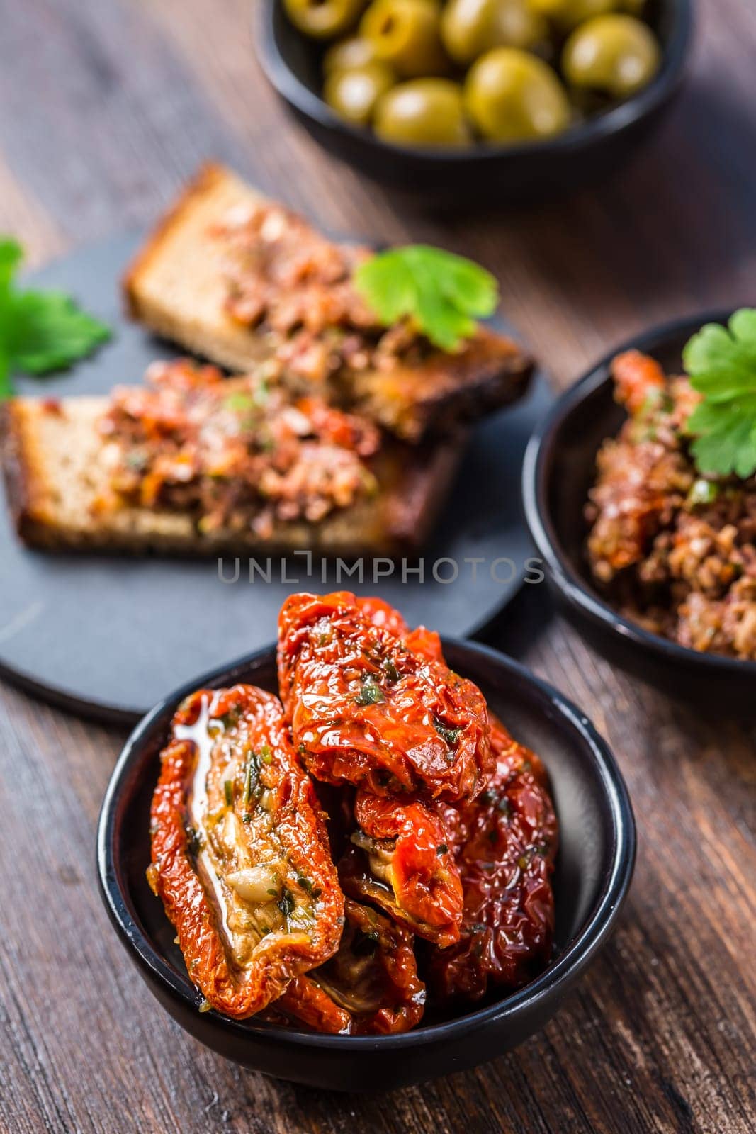 Sun dried tomatoes in olive oil and crostini with tapenade and ingredients. Tapenade - delicious olive paste, French cuisine