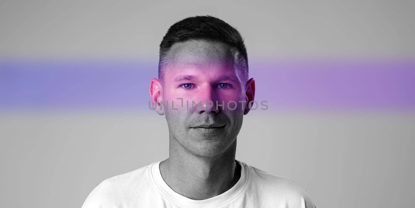 A man stands confidently in a creative studio environment, illuminated by vibrant light effects. His relaxed expression and unique backdrop emphasize modern artistic themes.