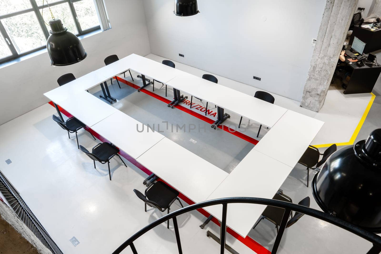 Bright conference room featuring a long rectangular table with a central channel, surrounded by black chairs and industrial-style lighting fixtures.
