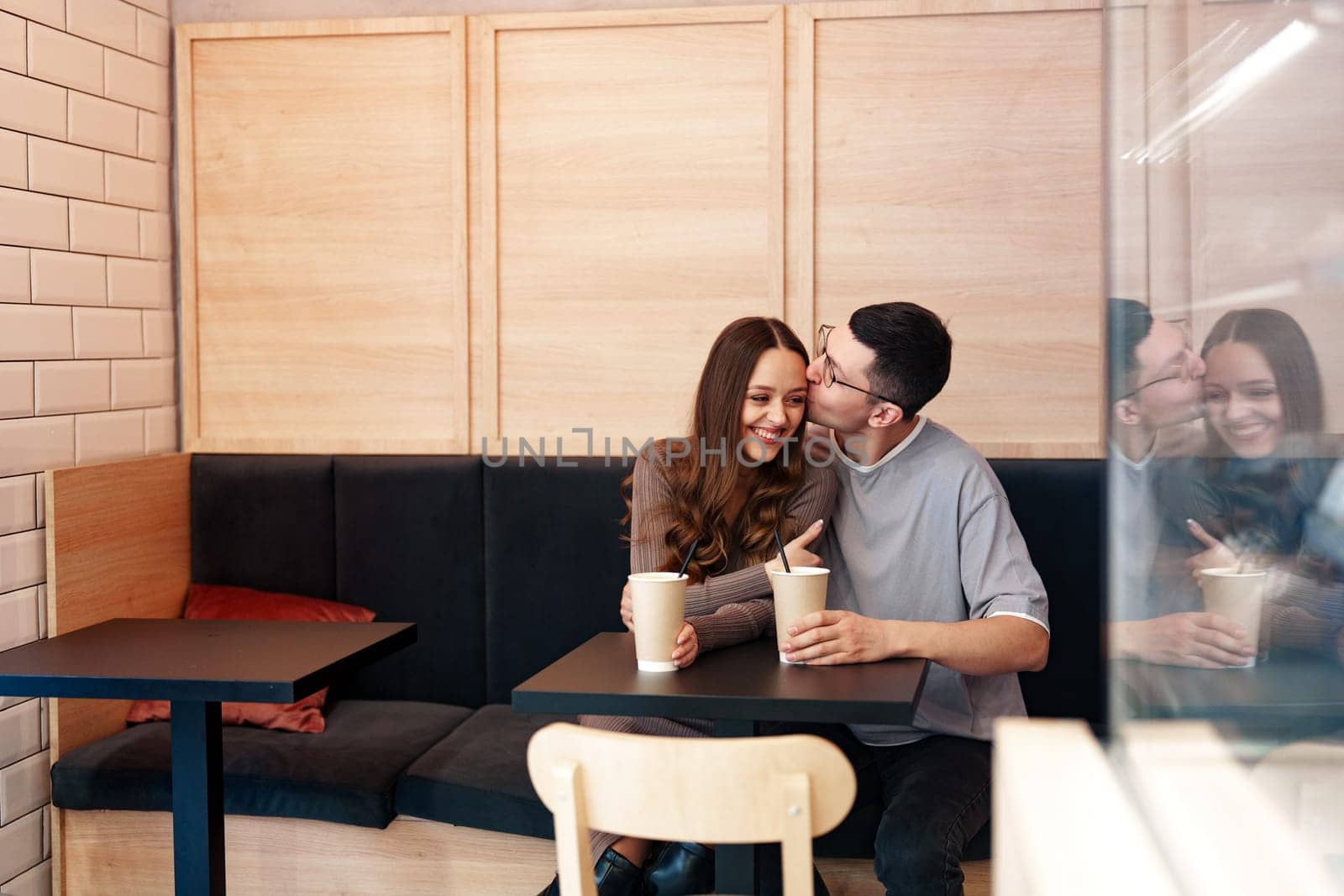 Two young individuals share a joyful moment in a modern cafe, sipping their drinks and smiling at each other. The inviting atmosphere enhances their connection.