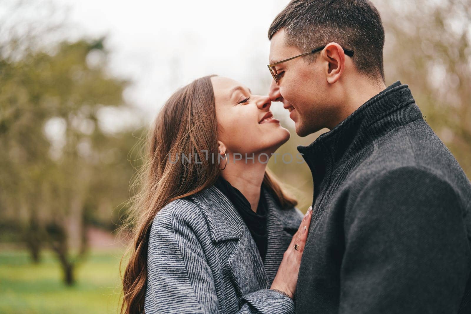A man and woman share a warm embrace in a lush park. Their smiles convey joy and affection as they gaze into each other's eyes amidst the greenery, highlighting a moment of connection.